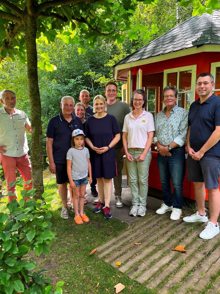 Gruppe von Menschen vor rotem Gartenhäuschen in fröhlicher Atmosphäre.