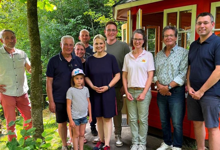 Gruppe von Menschen vor rotem Gartenhäuschen in fröhlicher Atmosphäre.